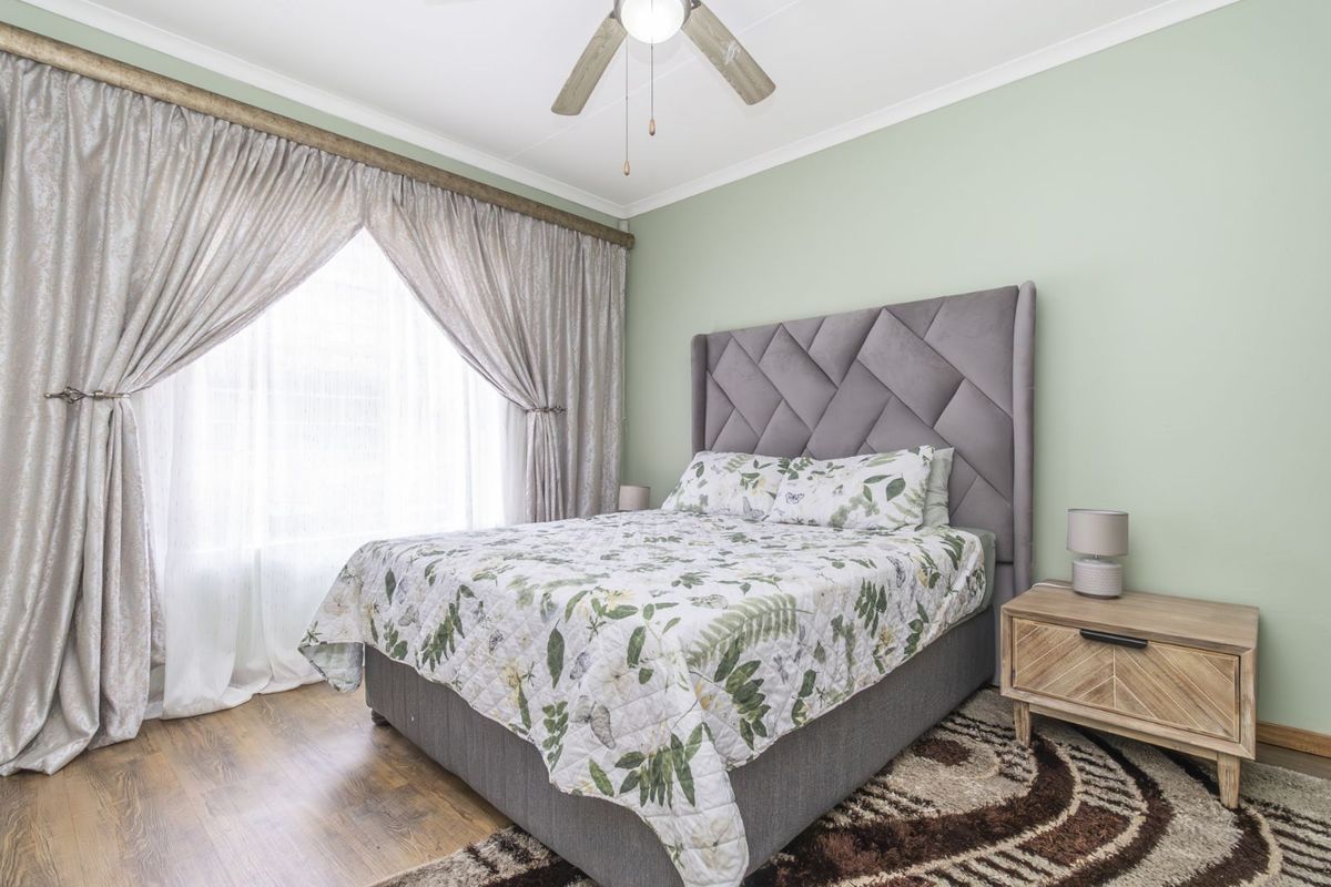 A well-maintained bedroom featuring laminate flooring, a ceiling fan, and large windows with curtain tracks.
