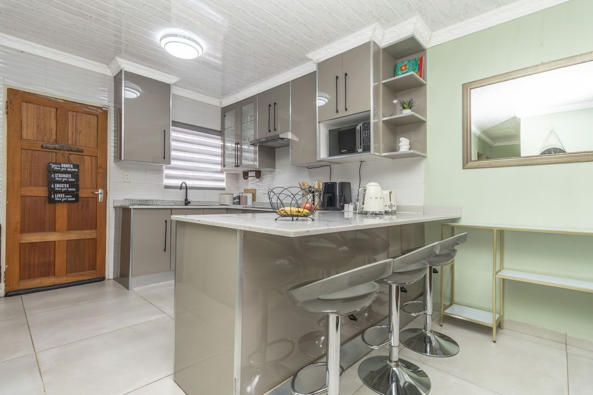 Modern kitchen featuring high-gloss cabinetry, stone-look countertops, a breakfast bar, and integrated microwave, finished with tiled flooring and a clean, contemporary aesthetic.