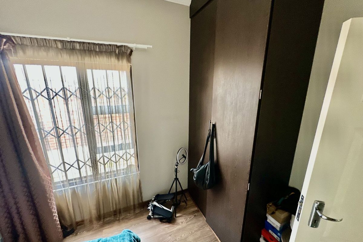 A bedroom featuring dark wood-finish built-in cupboards and a window fitted with a security gate.