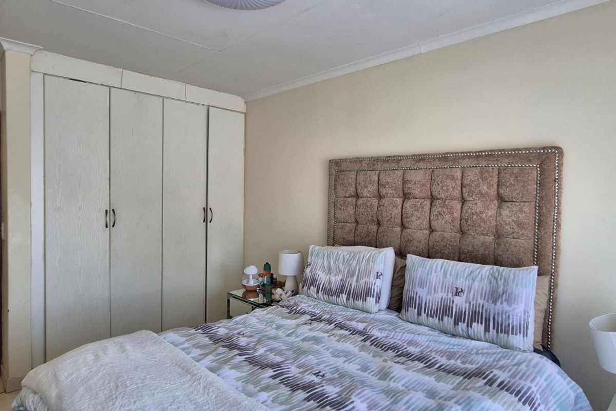 A bedroom featuring built-in cupboards and an adjacent tiled bathroom, offering a functional layout with neutral finishes.