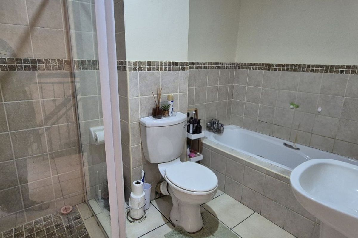 A functional bathroom featuring a tiled shower enclosure, a bathtub, a pedestal sink, and a standard toilet with neutral wall tiling.