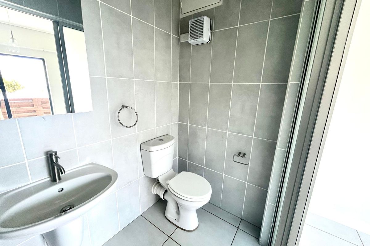 A modern bathroom featuring grey wall and floor tiles, a pedestal basin, a toilet, and an integrated extractor fan.