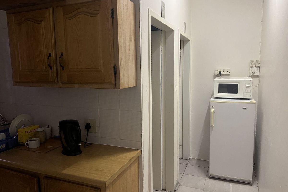 A functional office kitchenette featuring wooden cabinetry, tiled splashbacks, and tiled flooring, providing essential utility space for staff.