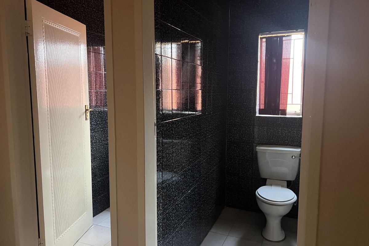 A functional office restroom featuring dark tiled walls, a standard white toilet, and a small window for natural light.