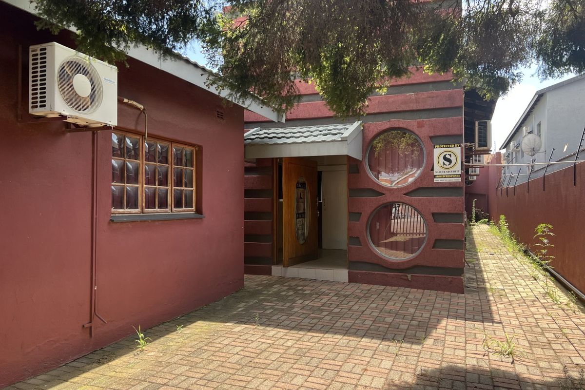 Exterior view of the office building entrance featuring unique circular windows, paved courtyard area, and wall-mounted air conditioning unit.