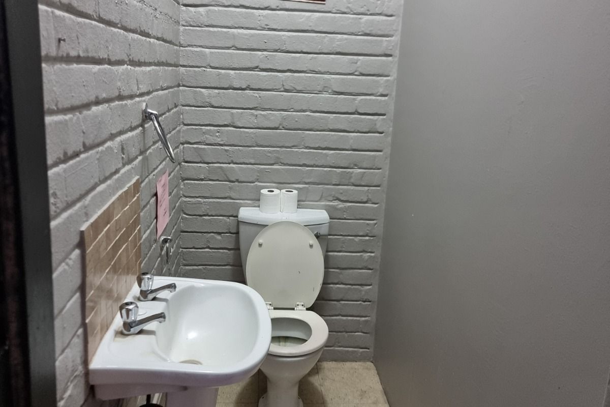 A compact commercial restroom featuring a pedestal sink and a standard toilet, finished with painted brick walls and tiled flooring.