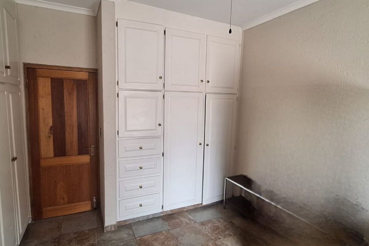 A bedroom featuring built-in white cabinetry with integrated drawers and a wooden door, finished with tiled flooring.