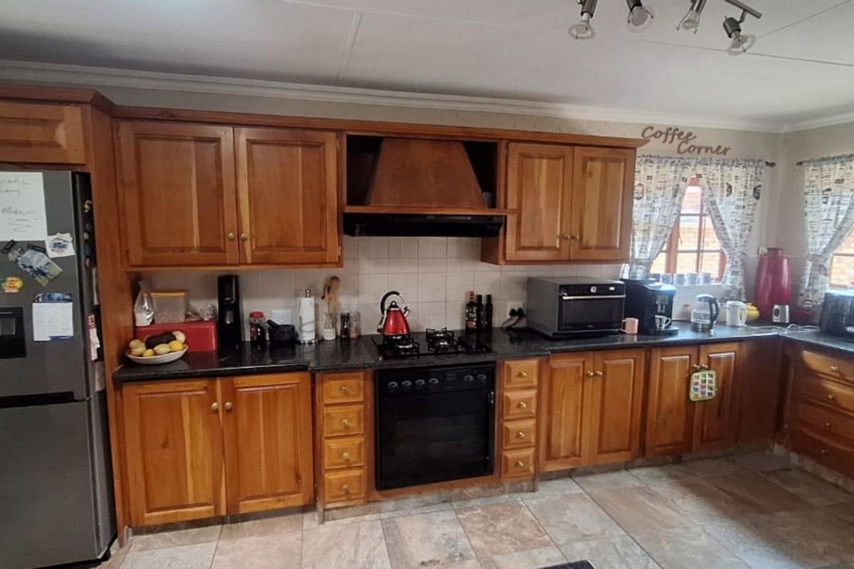 A functional kitchen featuring wooden cabinetry, dark countertops, a built-in oven, hob, and extractor fan, with tiled flooring throughout.