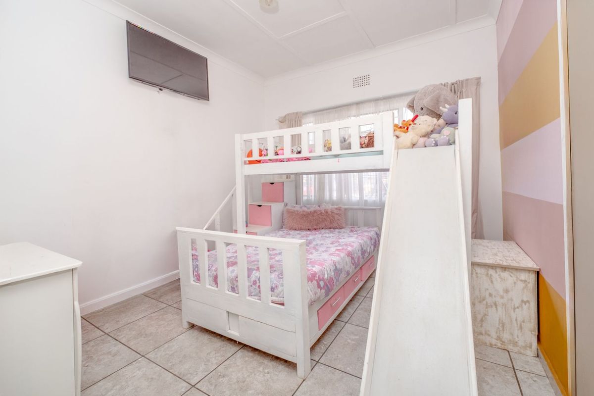 A bedroom featuring tiled flooring, a wall-mounted television, and a window with curtains.