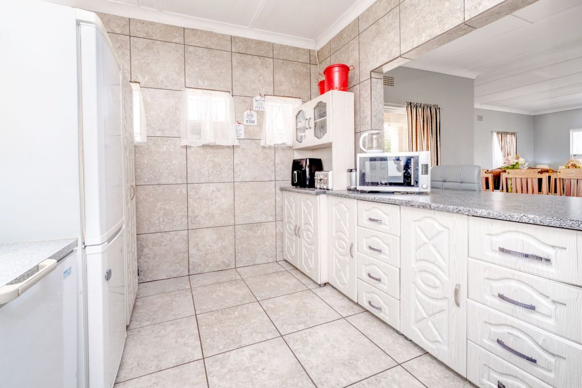 A functional kitchen featuring tiled walls and flooring, white cabinetry with decorative detailing, and a granite-look countertop.