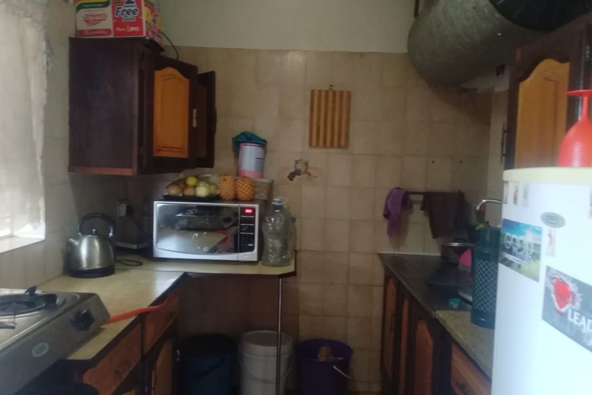 A compact kitchen featuring dated wooden cabinetry, tiled splashbacks, and integrated ventilation ducting, providing a functional but aged culinary workspace.