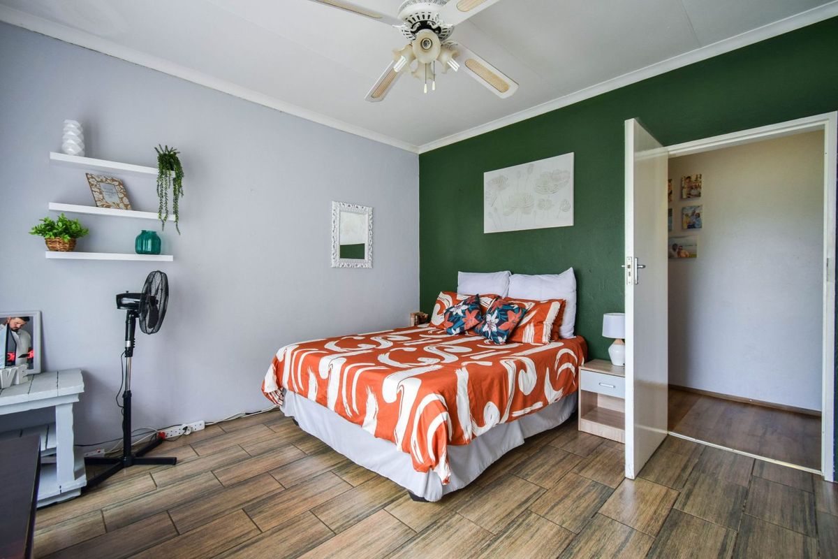 A bedroom featuring wood-look tiled flooring, a ceiling fan, and a contrasting green accent wall.