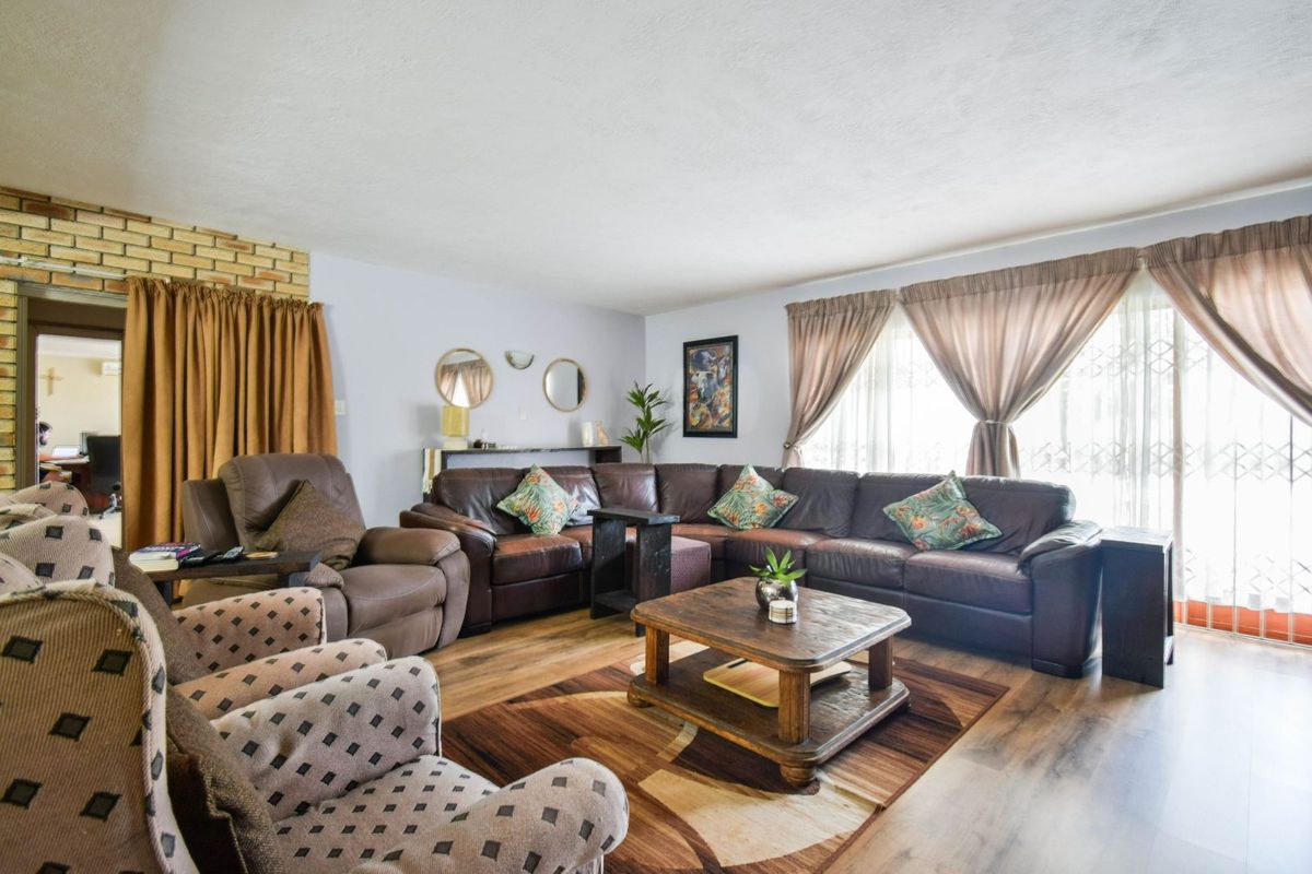 A spacious living room featuring wood-look laminate flooring, a brick accent wall, and large sliding glass doors with security gates leading to the exterior.
