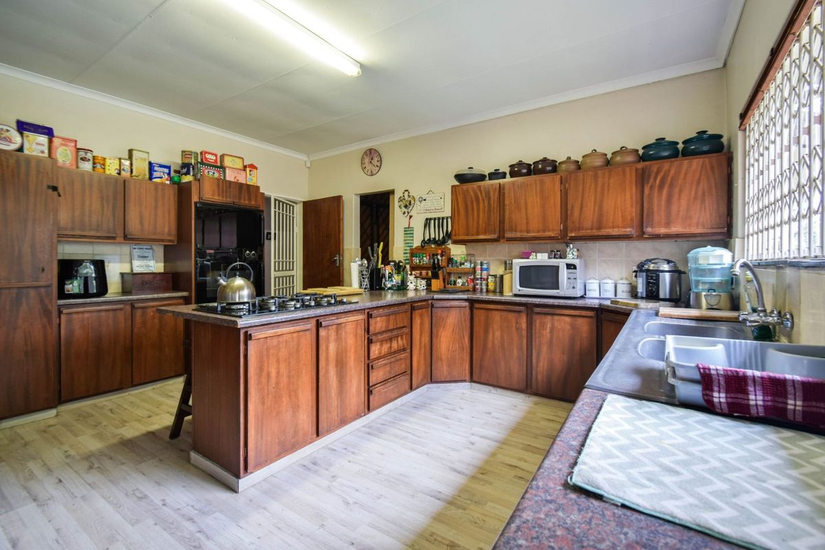 A functional kitchen featuring extensive wooden cabinetry, laminate countertops, a built-in gas hob, and a double stainless steel sink.