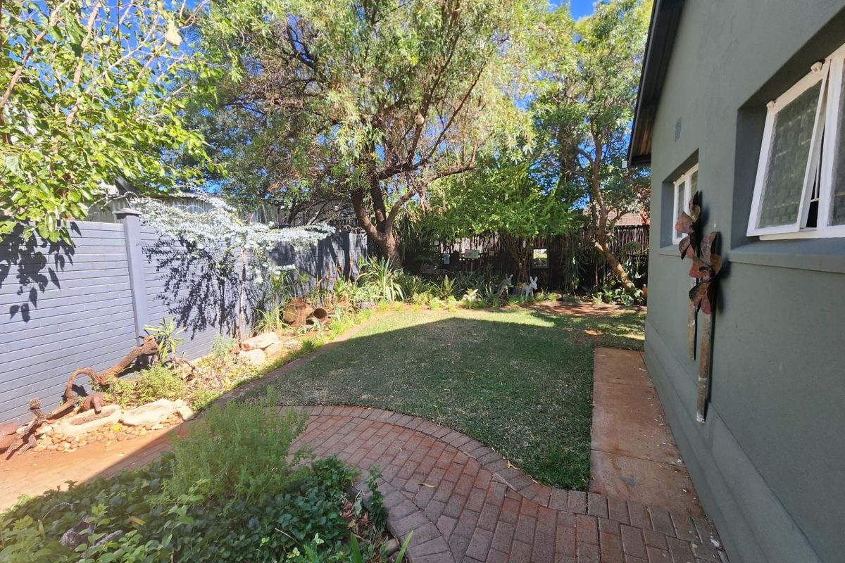 A well-maintained rear garden featuring a brick-paved pathway, manicured lawn, established trees, and perimeter fencing, providing a private outdoor space.