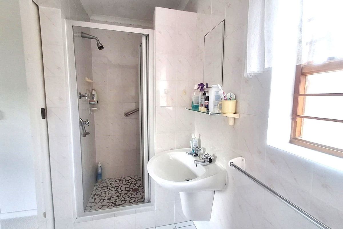 A functional bathroom featuring a glass-enclosed shower, a wall-mounted pedestal basin, and tiled finishes throughout.