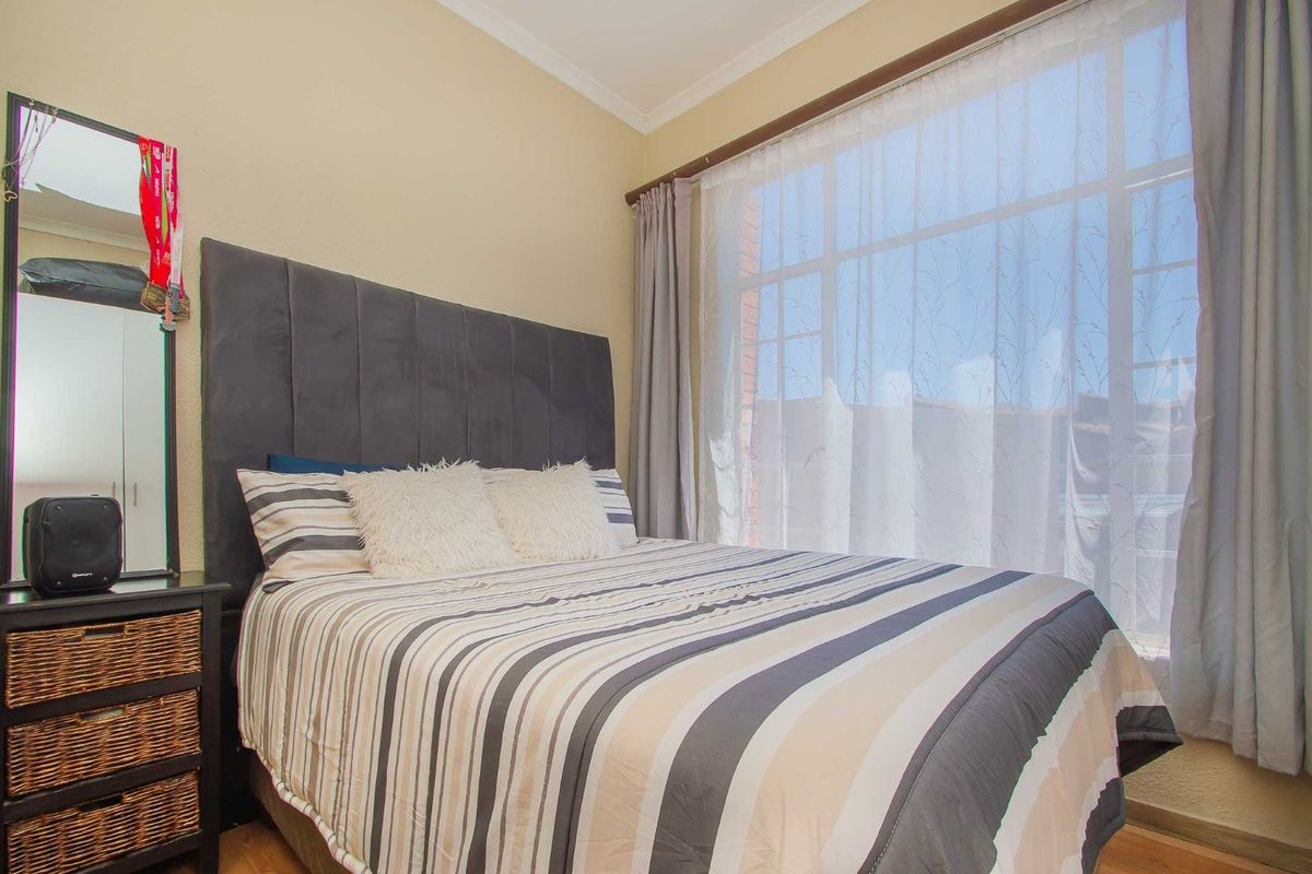 A cozy bedroom featuring a large window with curtains, providing natural light and a neutral wall finish.