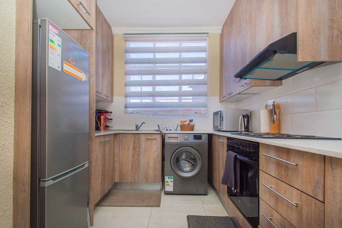 Compact kitchen featuring wood-look cabinetry, tiled splashbacks, integrated oven and hob, and dedicated space for a washing machine.