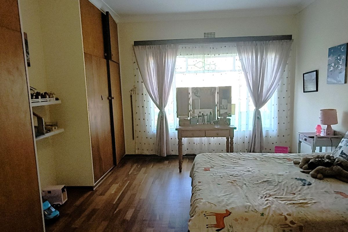 A bedroom featuring built-in wooden cupboards, timber flooring, and a large window with natural light.