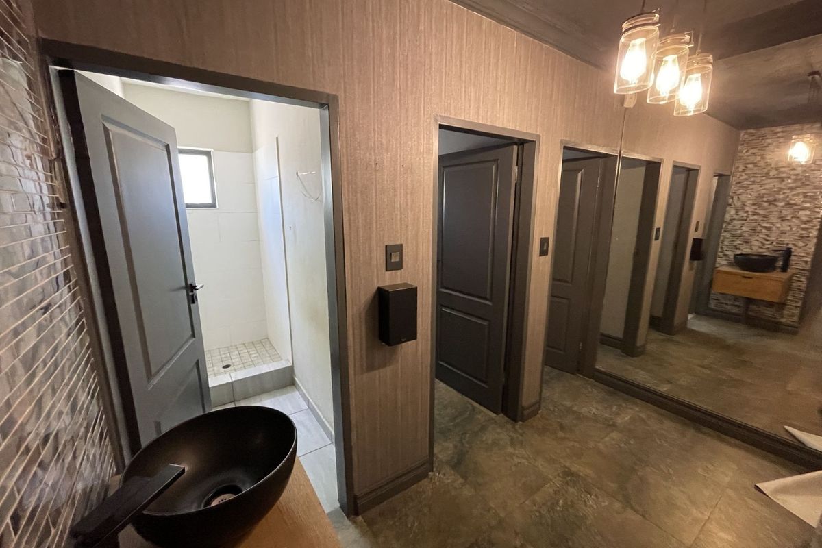 A modern bathroom area featuring multiple doorways, a vessel sink vanity, large wall mirror, and tiled flooring with contemporary lighting fixtures.