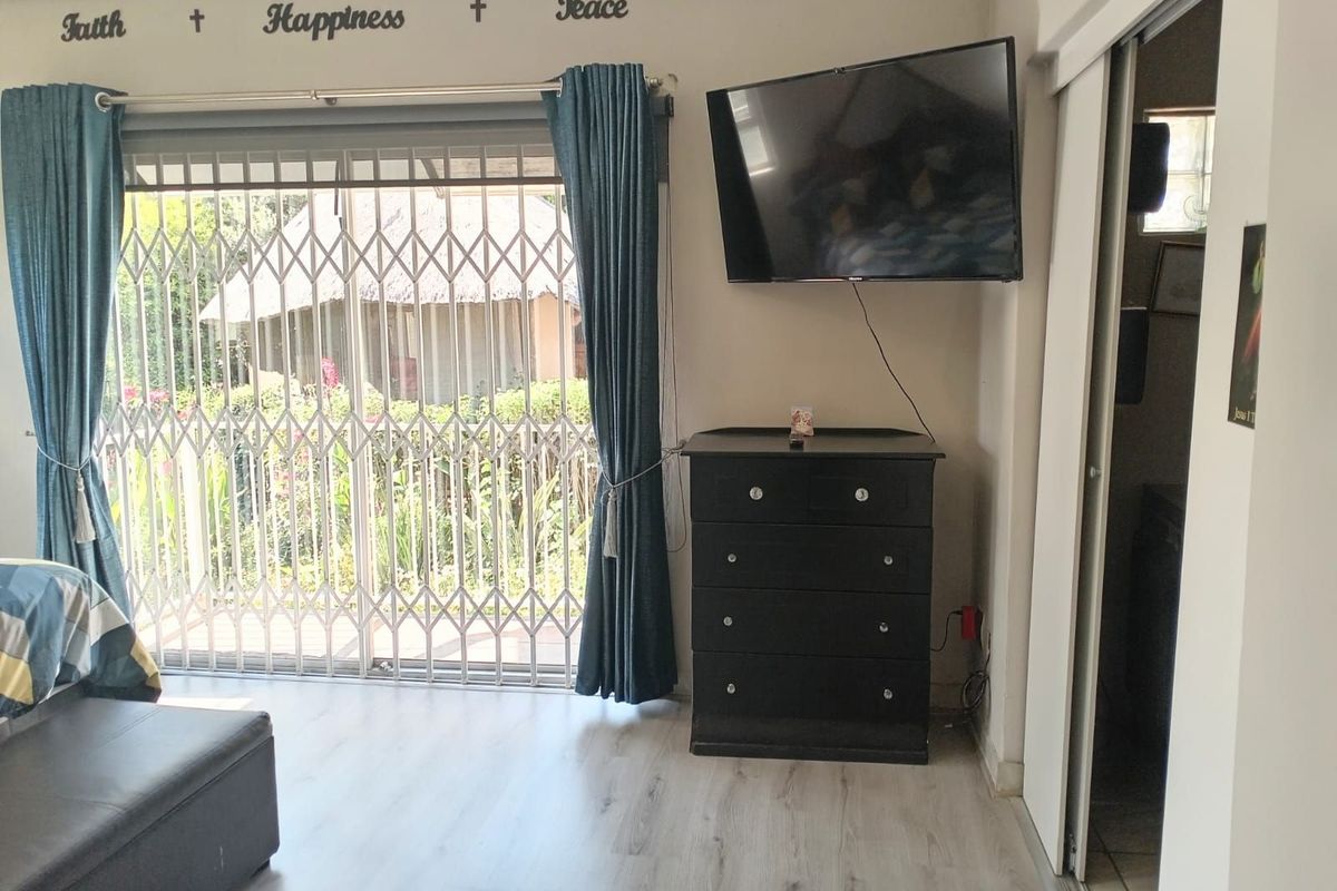 A living area featuring light-toned laminate flooring, a sliding glass door with security gate, and direct access to an outdoor space.
