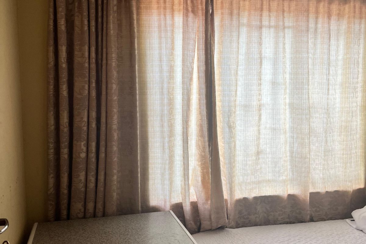 A bedroom featuring a window with curtains and a built-in chest freezer, showing signs of wear on the ceiling and wall finishes.
