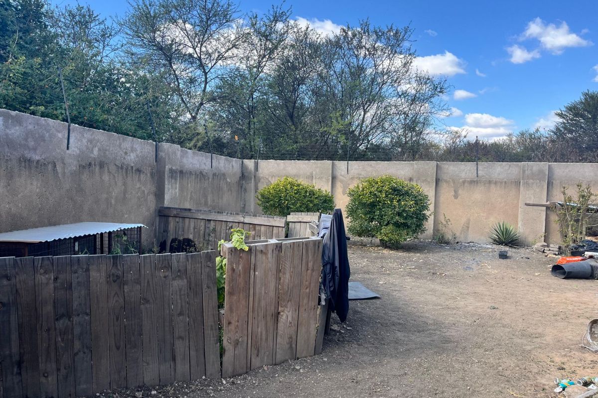 A spacious rear garden area featuring a high perimeter boundary wall and existing wooden enclosure structures, offering potential for landscaping and outdoor development.
