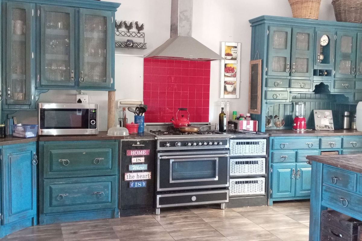 A rustic-style kitchen featuring blue painted cabinetry, a stainless steel range cooker with extractor hood, and a vibrant red tiled splashback.