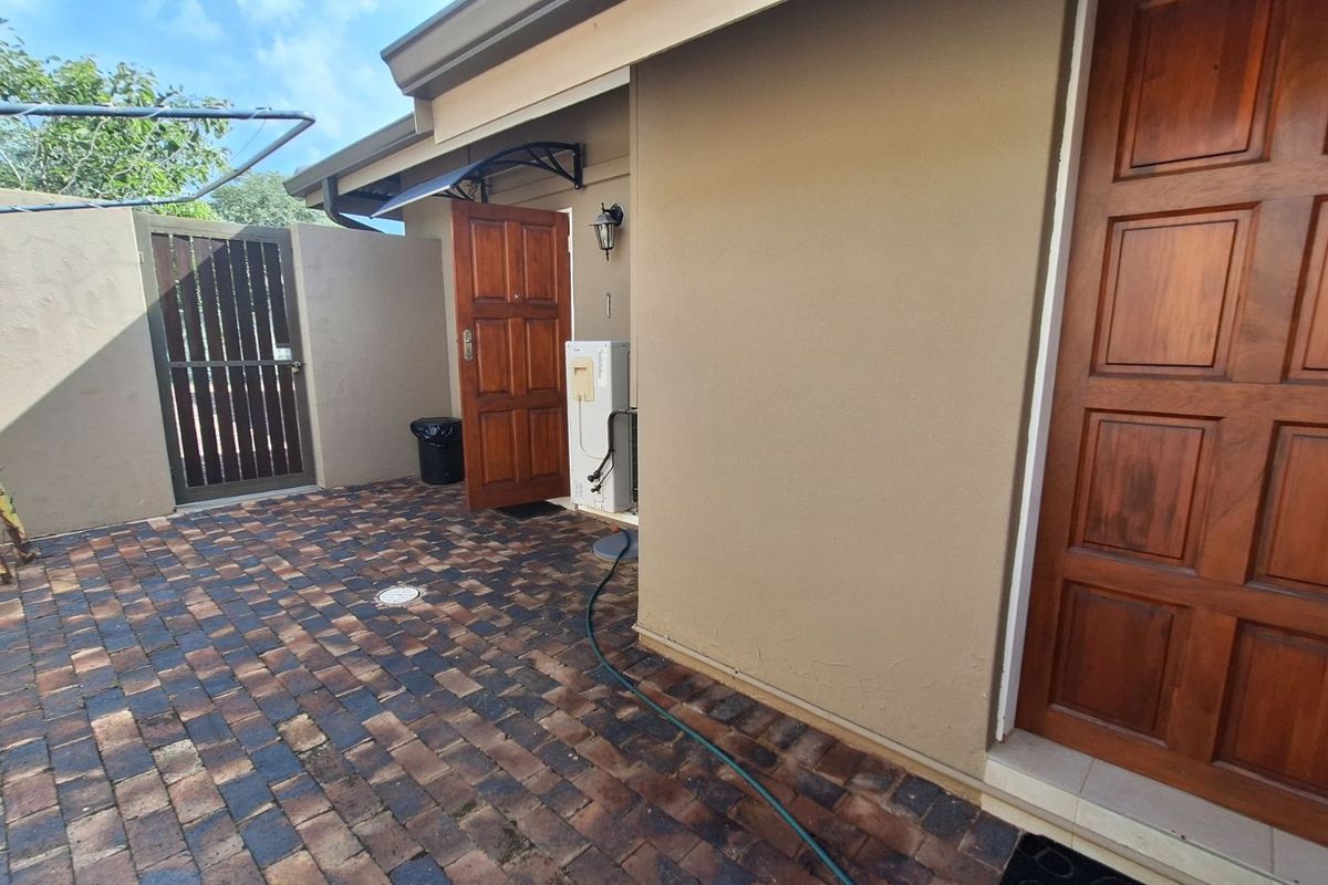 A paved rear courtyard area featuring a wooden door entrance, security gate, and exterior wall-mounted lighting.
