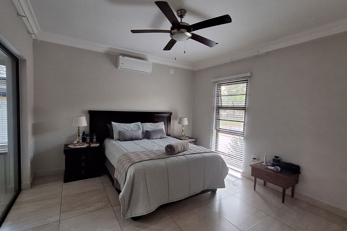 A well-maintained bedroom featuring tiled flooring, a ceiling fan, and a wall-mounted air conditioning unit, with large sliding doors providing natural light.
