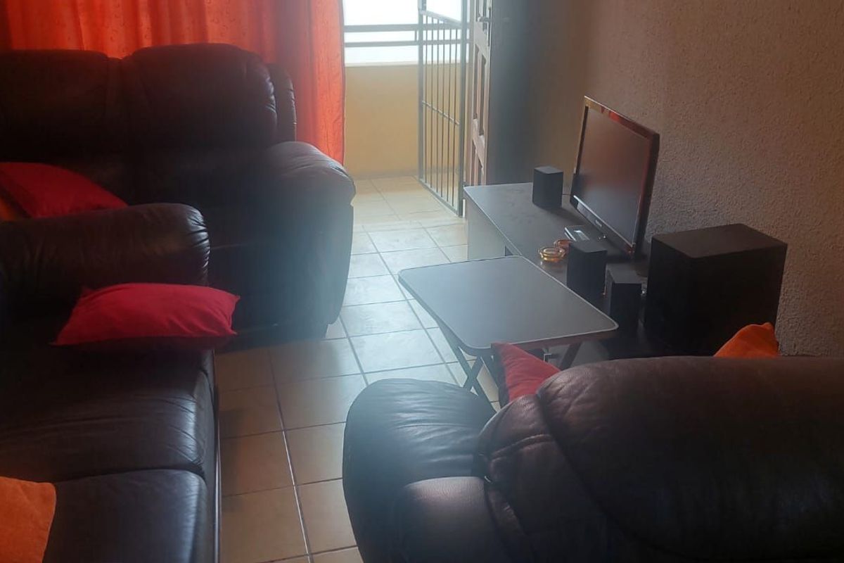 A living room area featuring tiled flooring and direct access to an outdoor balcony through a security gate and sliding door.