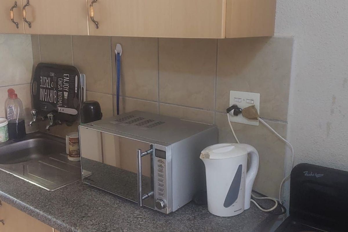A compact kitchen area featuring laminate cabinetry, a stainless steel sink, and tiled splashbacks, showing signs of wear and dated finishes.