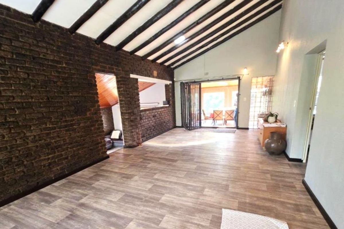 Spacious living area featuring exposed timber ceiling beams, a rustic face-brick feature wall, and sliding doors leading to an outdoor patio.