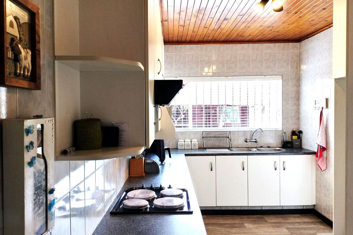 A functional kitchen featuring white cabinetry, dark countertops, a built-in hob, and a double sink with a window view.