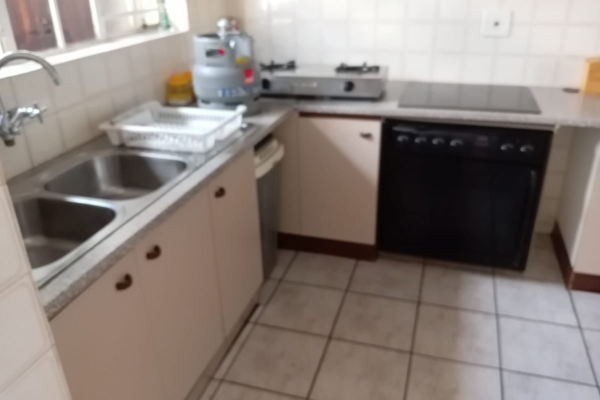 A functional kitchen featuring a double stainless steel sink, built-in oven, and hob with tiled splashbacks and neutral cabinetry.