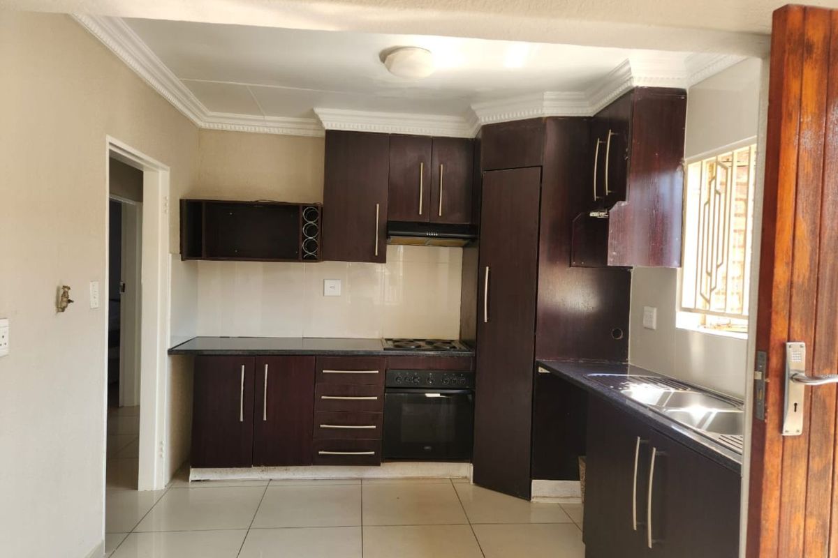 A functional kitchen featuring dark wood cabinetry, built-in oven, hob, extractor fan, and a double stainless steel sink with tiled flooring.