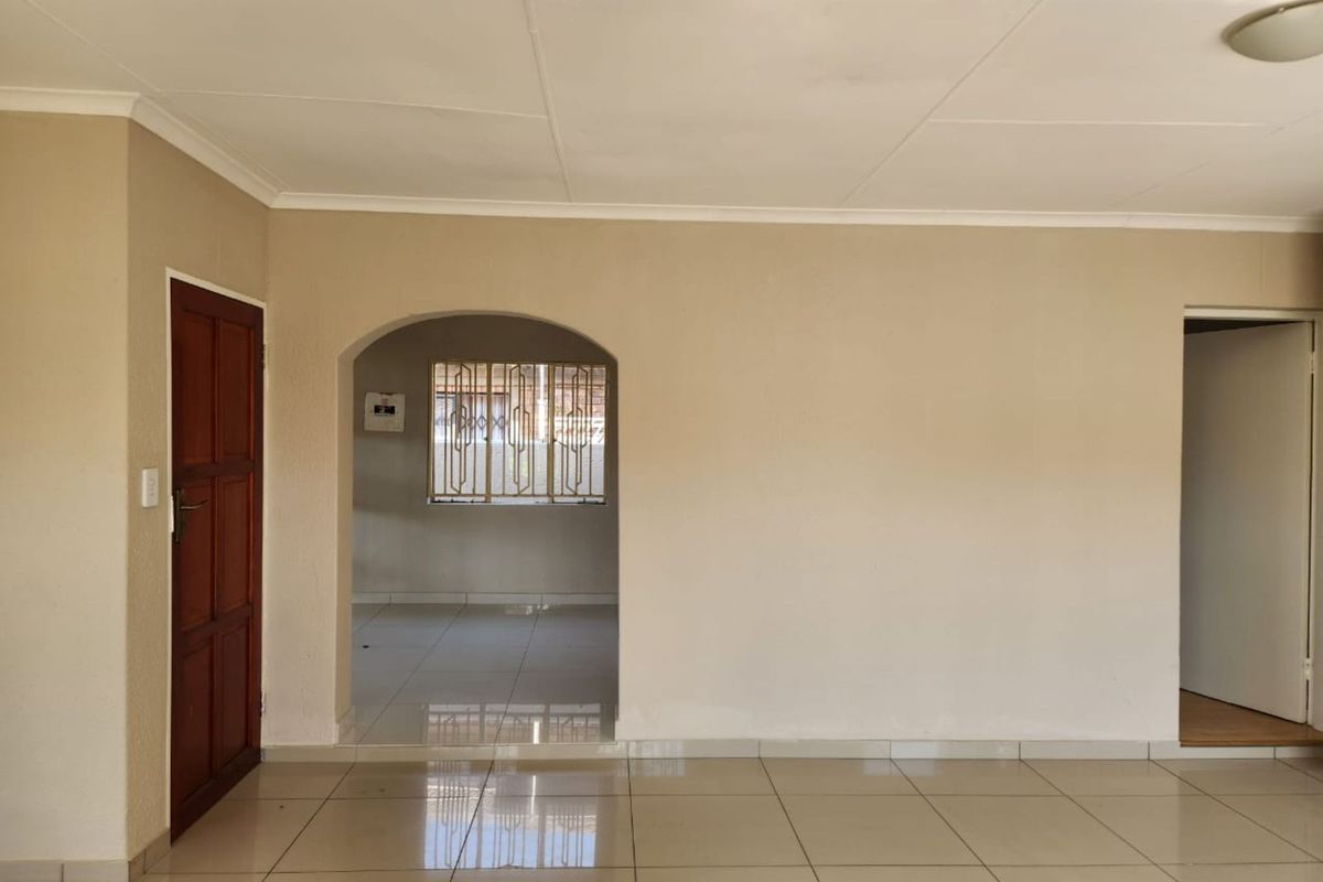 A bright, empty living area featuring neutral tiled flooring, an arched entryway, and a wooden door, offering a clean canvas for personalization.