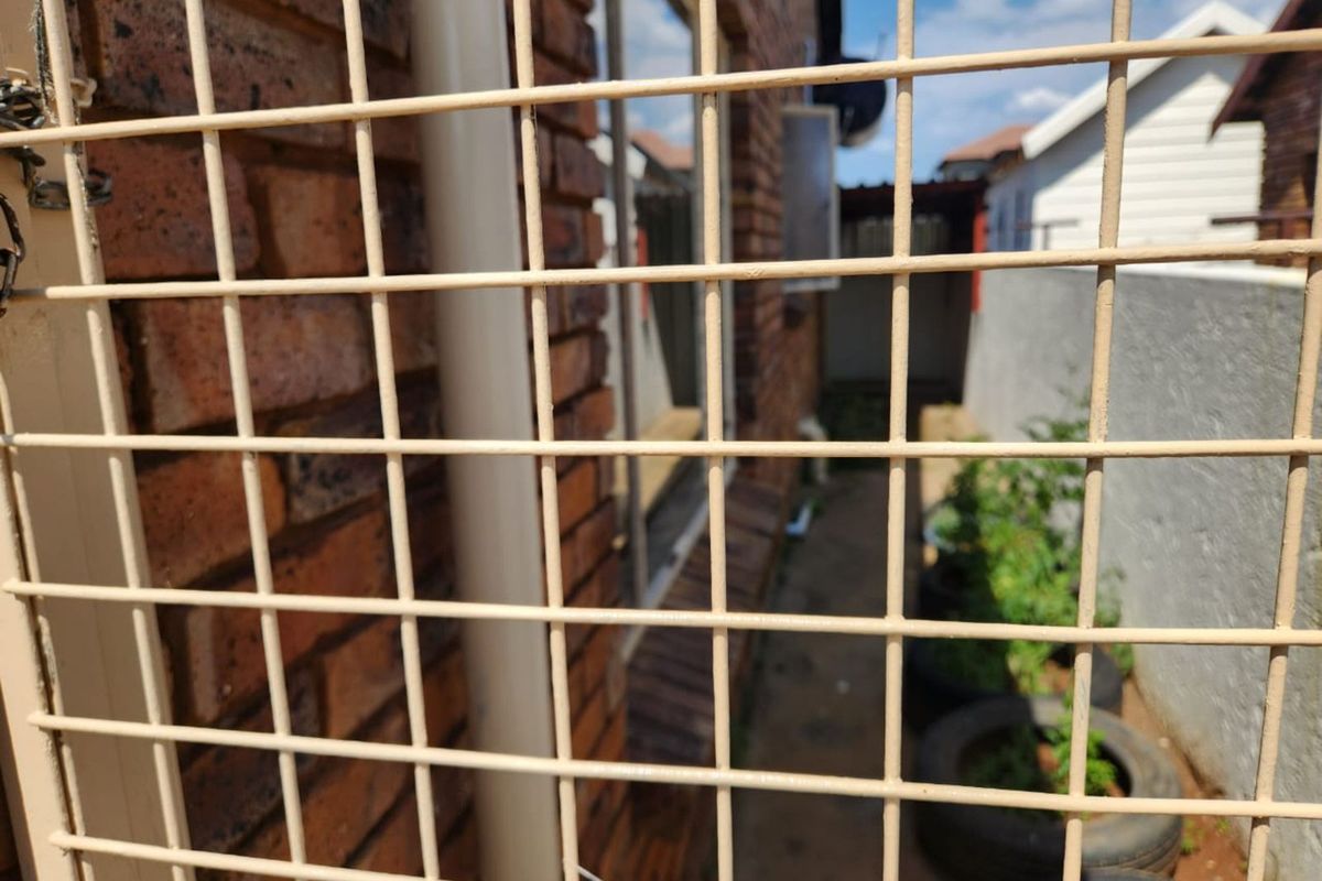 A narrow side passage of the property featuring exposed brick walls, a downpipe, and a metal security gate.