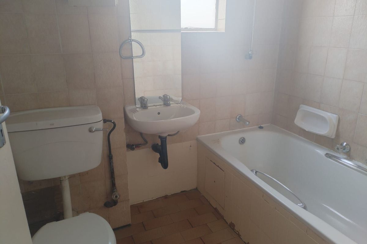 A dated bathroom featuring a standard bathtub, wall-mounted basin, and toilet, with original wall tiling and exposed plumbing fixtures.