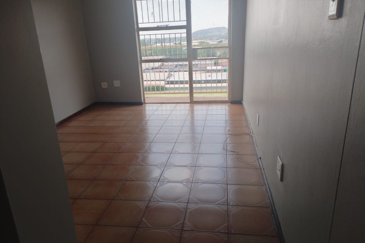An empty bedroom featuring tiled flooring, neutral walls, and a sliding glass door providing access to a balcony with an urban view.