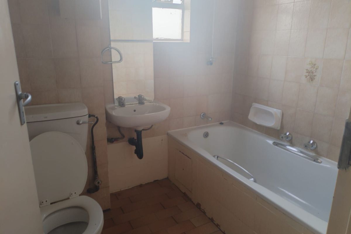 A dated bathroom featuring a standard bathtub, wall-mounted basin, and toilet, with original wall and floor tiling in need of modernization.