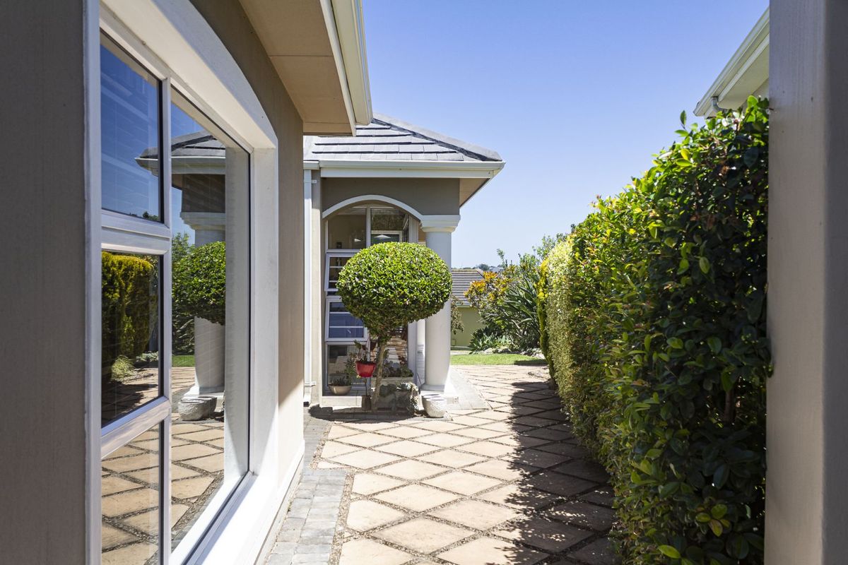 A well-maintained paved side walkway featuring a manicured hedge, leading towards a covered patio area with classic architectural columns.