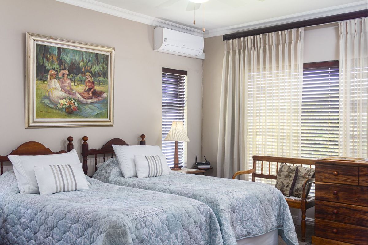 A well-maintained bedroom featuring a wall-mounted air conditioning unit, crown molding, and large windows with fitted blinds and curtains.