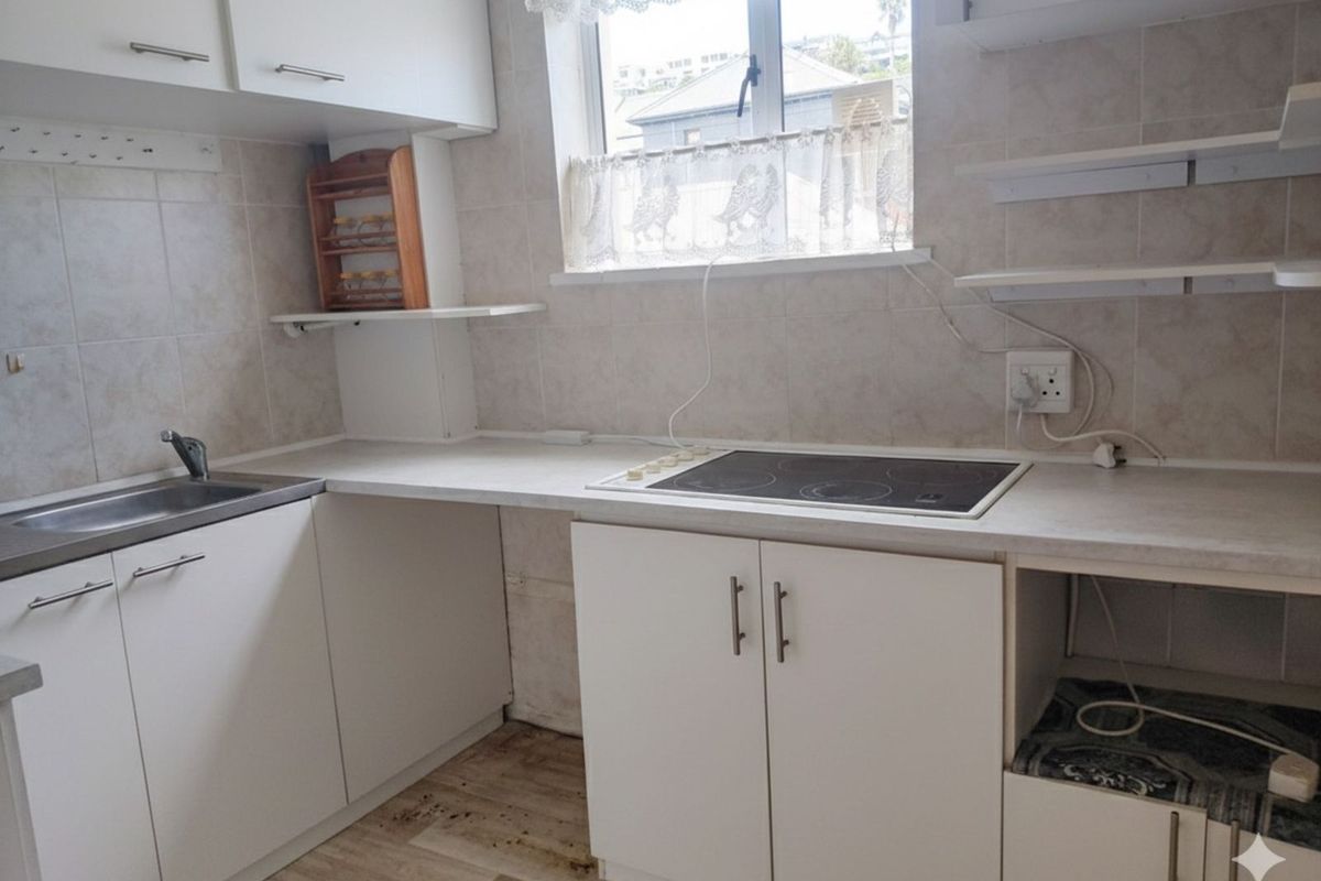 A compact kitchen featuring white cabinetry, a built-in electric hob, and a stainless steel sink with tiled splashbacks.