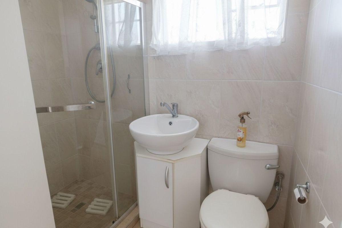 Compact bathroom featuring a glass-enclosed shower, a modern vessel sink vanity, and a standard toilet with neutral wall tiling.