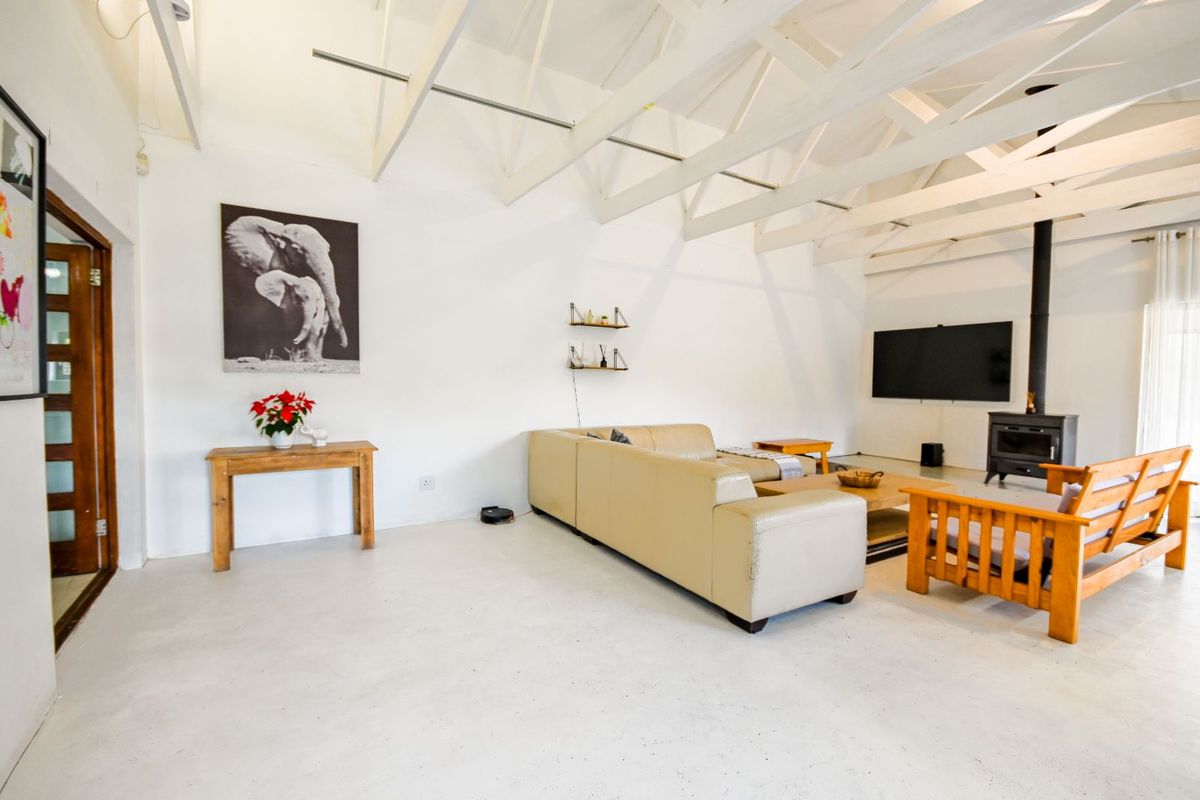 Spacious living area featuring exposed white timber roof trusses, polished concrete flooring, and a built-in wood-burning fireplace.