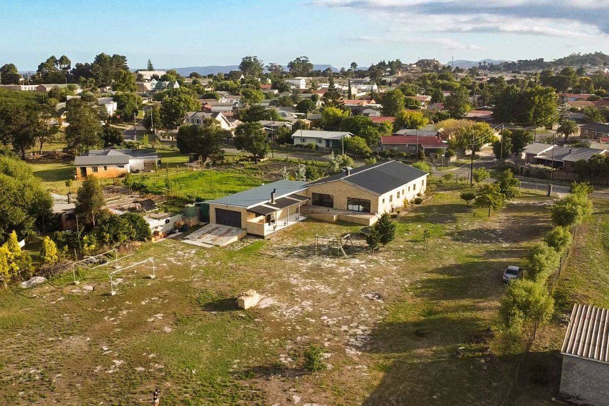 Aerial view of a residential property featuring a large plot, a main house with a metal roof, and a detached garage structure.