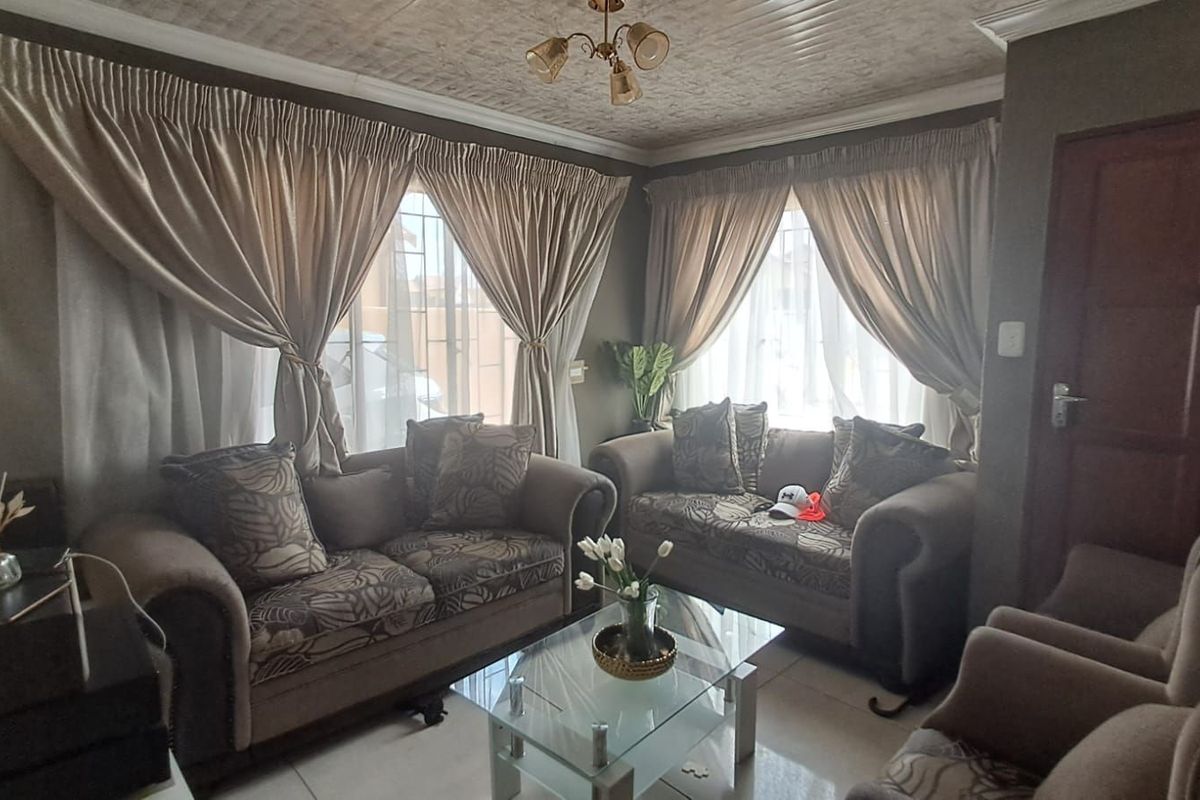A cozy living room featuring tiled flooring, large windows with curtains, and a decorative ceiling finish.