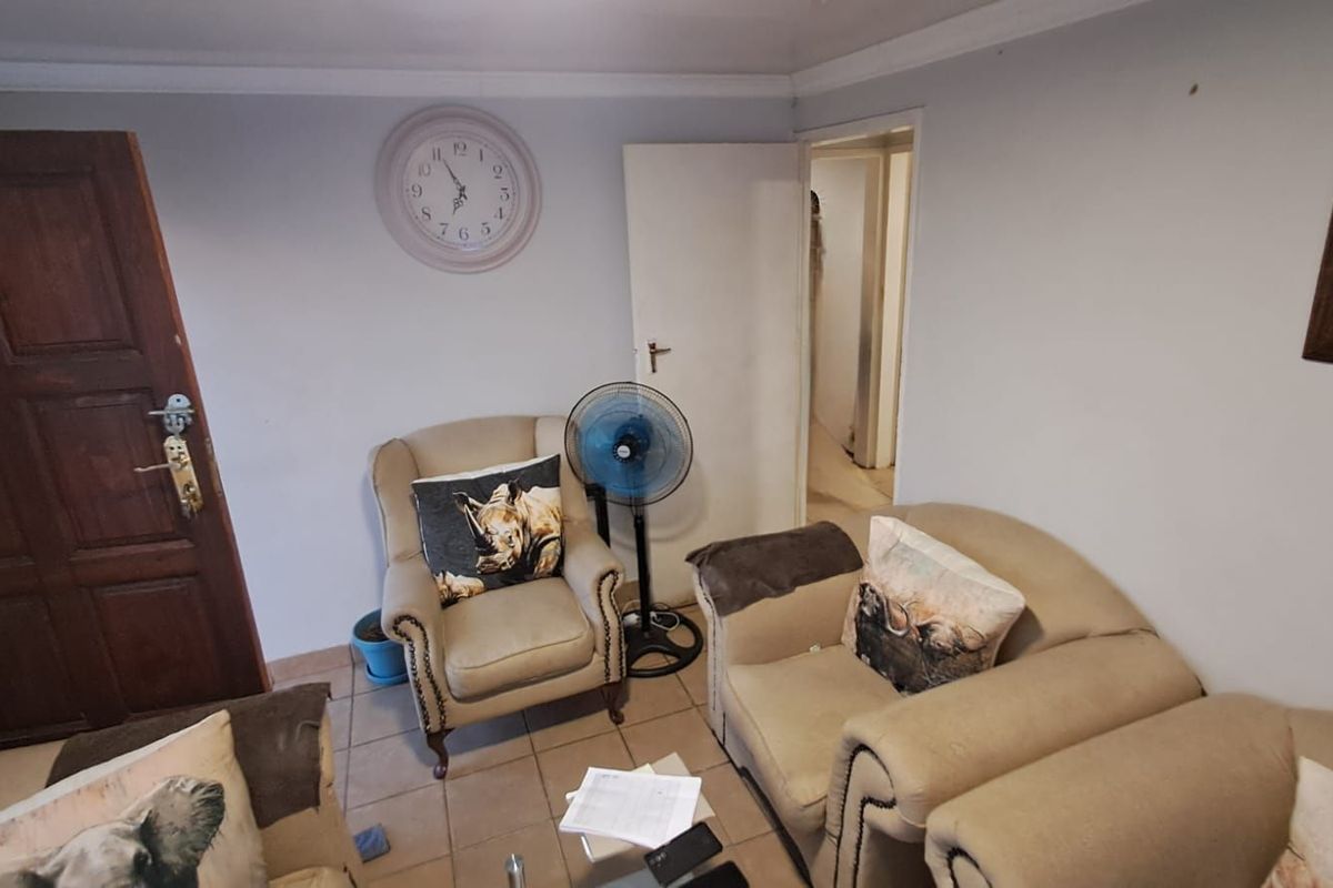 A living room area featuring tiled flooring, crown molding, and access to an adjacent hallway.
