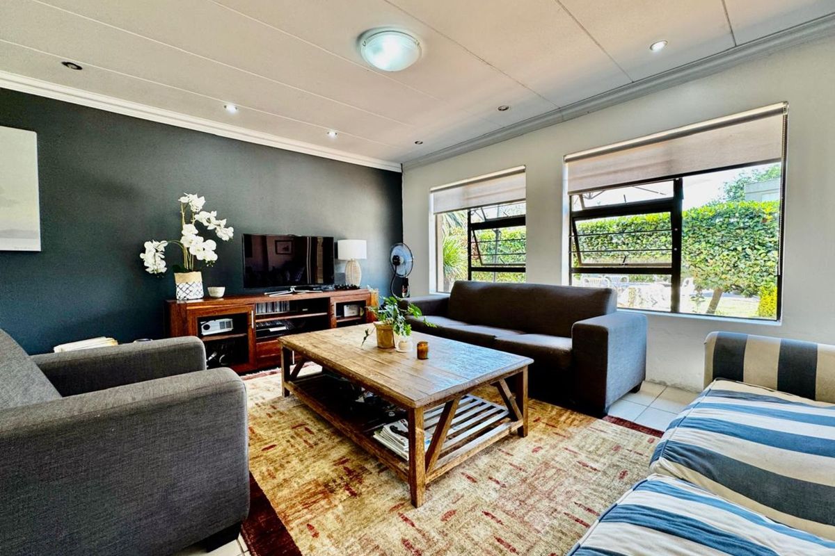 A comfortable living room featuring tiled flooring, recessed ceiling lighting, and large windows that provide natural light and views of the garden.